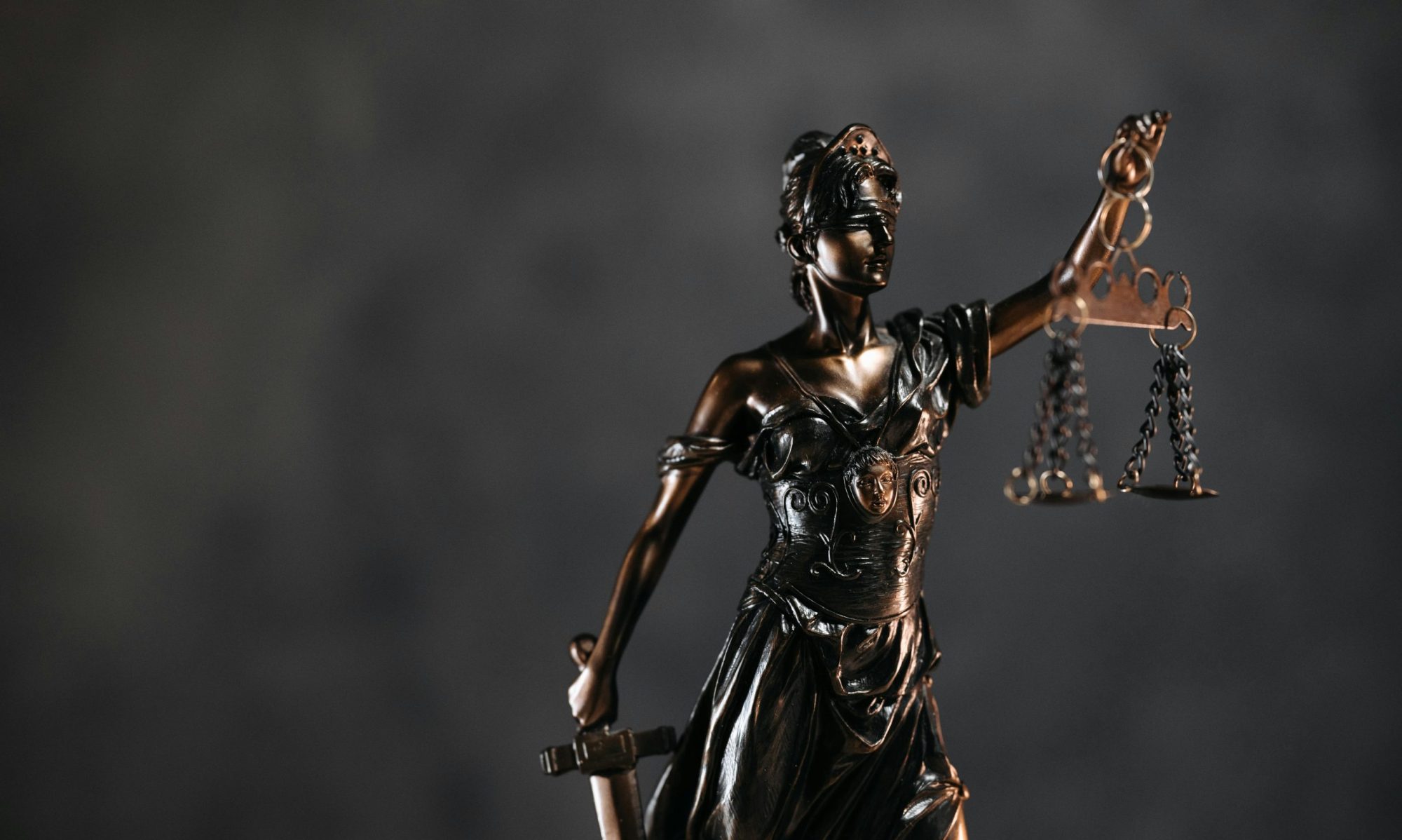 Detailed bronze Lady Justice statue with scales and sword against a dark background, symbolizing law and justice.